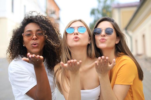 Three beauty women wearing summer clothes posing togeher in tke city and looking at the camera, sending kiss