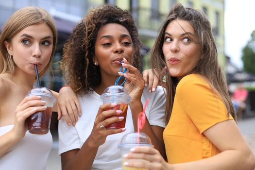 Three trendy cool hipster girls, friends drink cocktail in urban city background