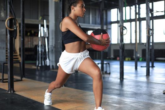Fit and muscular woman exercising with medicine ball at gym