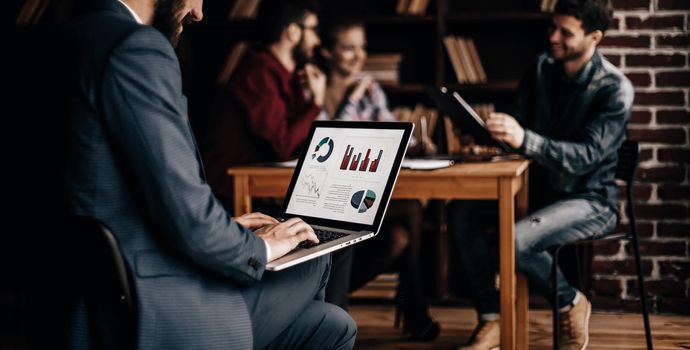 Manager Finance works with the marketing graphics on the laptop on the background of business team workplace in the office