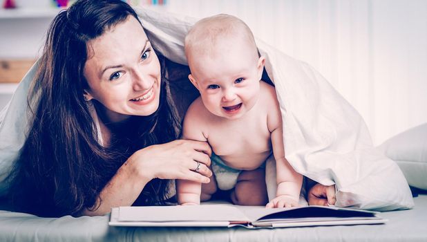 happy mother reading a book to her one year old child on the sofa in the nursery