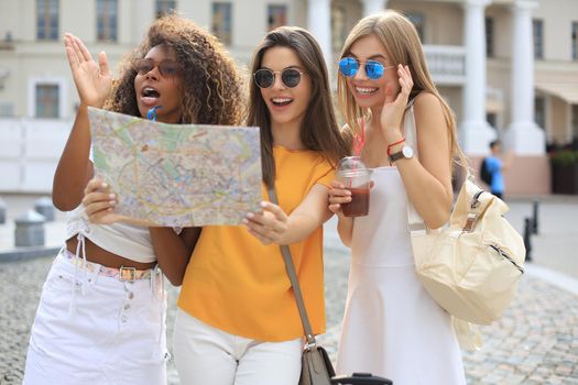 Photo of three girls enjoying sightseeing outdoor. Beautiful female tourists exploring city with map