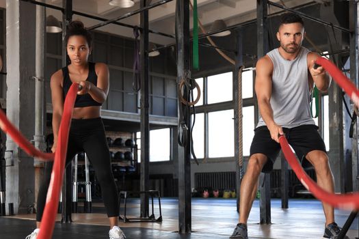 Athletic young couple with battle rope doing exercise in functional training fitness gym