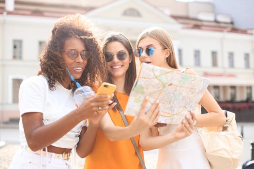 Photo of three girls enjoying sightseeing outdoor. Beautiful female tourists exploring city with map