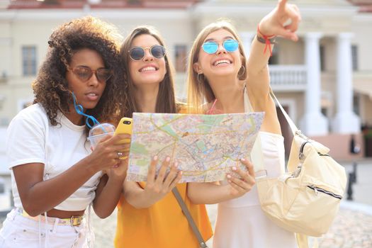 Photo of three girls enjoying sightseeing outdoor. Beautiful female tourists exploring city with map