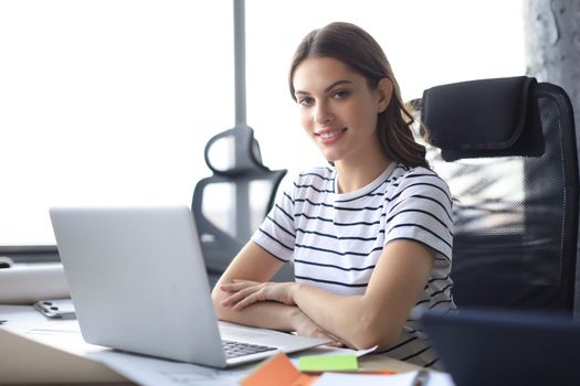 Beautiful young woman is sitting in the office and looking at camera