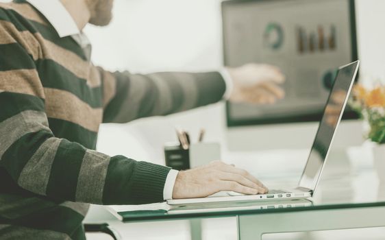 Finance specialist working on laptop with financial charts and marketing schemes in the modern office