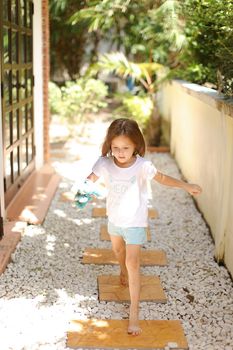 Little caucasian female kid walking barefoot on white gravel near exotic hotel. Concept of vacation with kid in Thailand, Phuket.