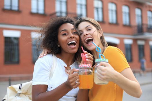 Trendy cool hipster girls, friends drink cocktail in urban city background