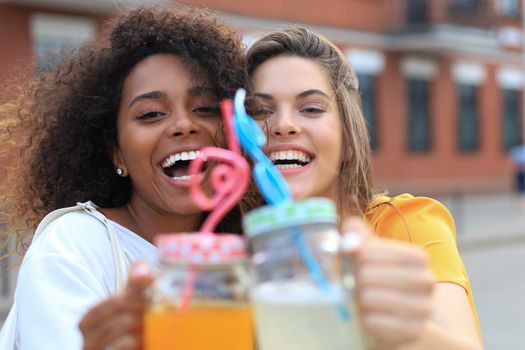 Trendy cool hipster girls, friends drink cocktail in urban city background