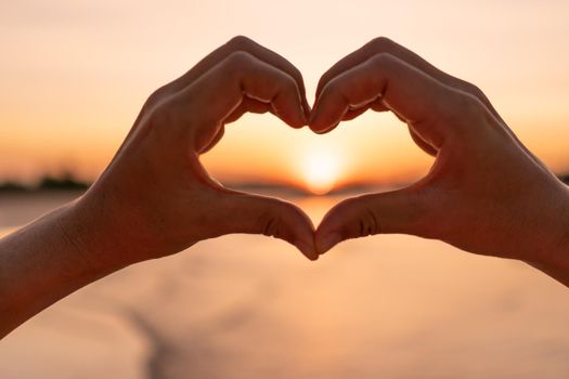 Woman hand do heart shape on sunset sky and bokeh background.