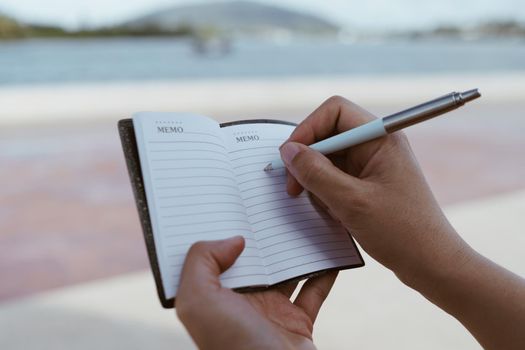 Woman hand writing down in small white memo notebook for take a note not to forget or to do list plan for future. 