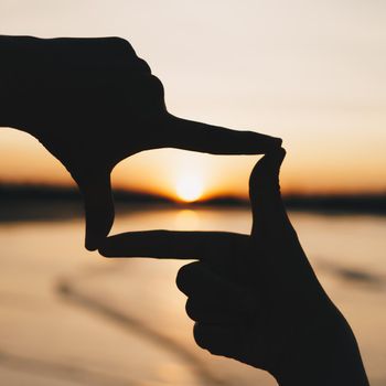 Woman hands place together like praying from nature in front of sunset beach background.