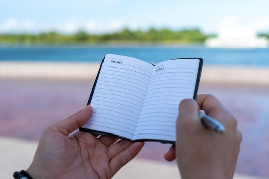 Woman hand writing down in small white memo notebook for take a note not to forget or to do list plan for future. 