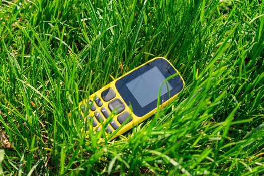 An outdated push-button mobile phone thrown into dense green grass, polluting nature