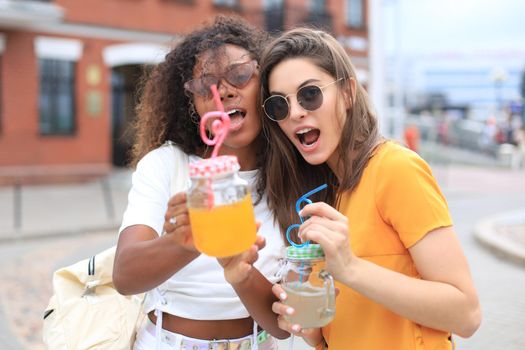 Trendy cool hipster girls, friends drink cocktail in urban city background