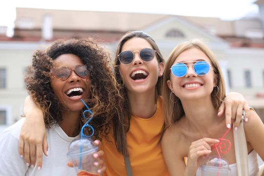 Three young smiling hipster women in summer clothes posing on street.Female showing positive face emotions