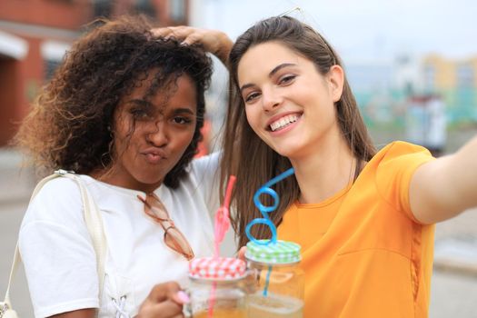 Two laughing friends enjoying weekend together and making selfie on city background