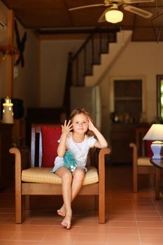 Little female kid sitting in chair with in living room. Concept of leisure time for children and wooden interior.