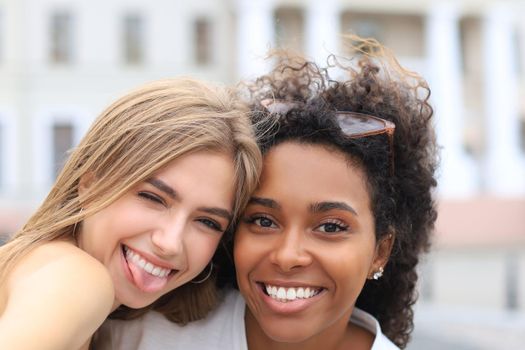 Young smiling hipster women in summer clothes posing on street.Female showing positive face emotions