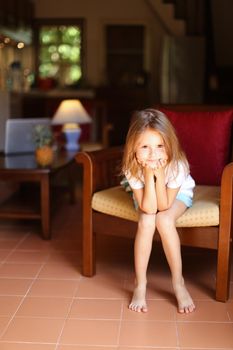 Female kid sitting in wooden chair in living room. Concept of child model and cozy interior.
