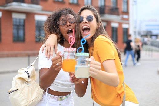 Trendy cool hipster girls, friends drink cocktail in urban city background