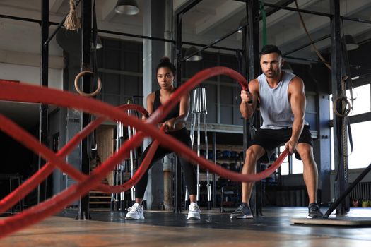 Athletic young couple with battle rope doing exercise in functional training fitness gym