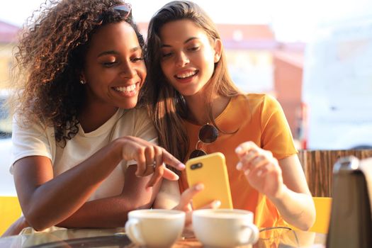 Two beautiful young woman sitting at cafe drinking coffee and looking at mobile phone