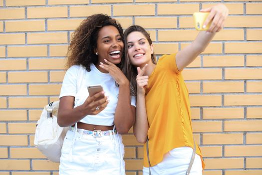 Two young smiling hipster women in summer clothes posing on street.Female showing positive face emotions