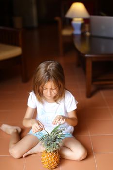 Little barefoot girl playing with pineapple and sitting on floor. Concept of health vegeterian lifestyle and children.