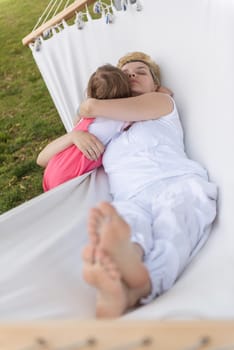 Happy mother and a little daughter enjoying free time hugging and relaxing in a hammock during a sunny day on holiday home garden