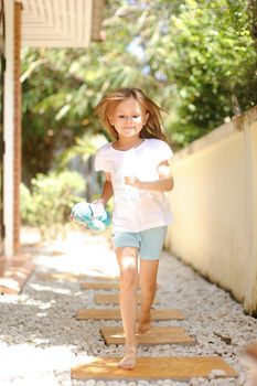 Little caucasian female kid running barefoot on white gravel near exotic hotel. Concept of vacation with kid in Thailand, Phuket.