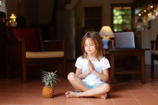 Little female kid sitting on floor with pineapple and meditating. Concept of health life, fruit and meditation.