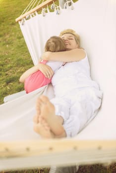 Happy mother and a little daughter enjoying free time hugging and relaxing in a hammock during a sunny day on holiday home garden