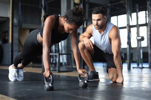 Sporty woman doing push-up in a gym, her boyfriend is watching her