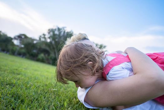 Young Mother and cute little daughter enjoying free time playing outside at backyard on the grass, happy family in nature concept