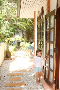 Little female kid standing near door with toy outside. Concept of resting with kids in Phuket, exotic hotel.