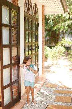 Little female kid standing near door with toy outside. Concept of resting with kids in Thailand, exotic hotel.