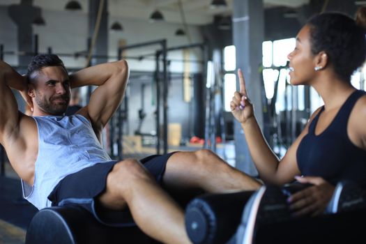 Trainer helping young man to do abdominal exercises in gym