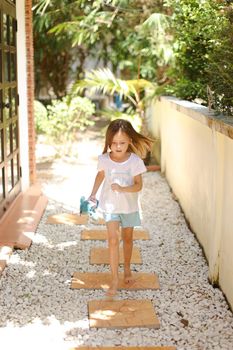 Little caucasian girl walking barefoot on white gravel near exotic hotel. Concept of vacation with kid in Thailand, Phuket.