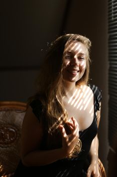 Portrait of young caucasian woman sitting in chair, striped shadows. Concept of female beauty and home photo session.