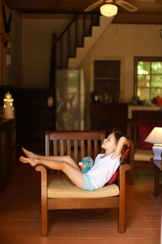 Little female child sitting in chair in living room. Concept of childhood and wooden interior.