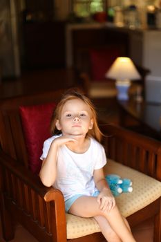 Little female kid sitting with toy in wooden chair. Concept of kid model and wood in interior.