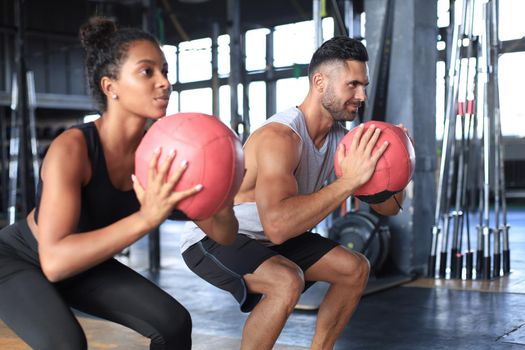 Beautiful young sports couple is working out with medicine ball in gym