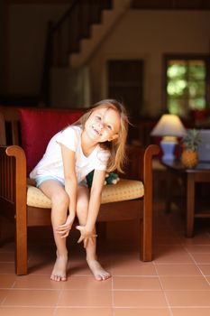 Little smiling female kid sitting with toy in wooden chair. Concept of kid model and wood in interior.