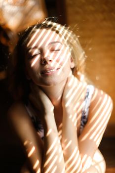 Portrait of young woman with closed eyes wearing bra, striped shadows. Concept of beautiful female person and home photosession.