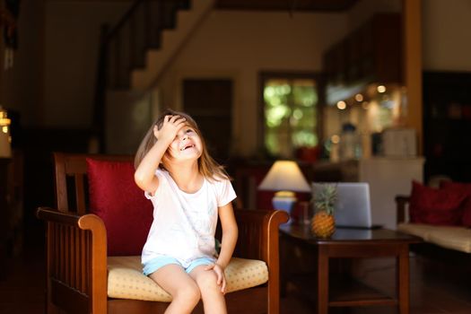 Female cute kid sitting in wooden chair in living room. Concept of child model and cozy interior.