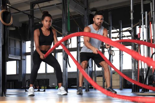 Athletic young couple with battle rope doing exercise in functional training fitness gym