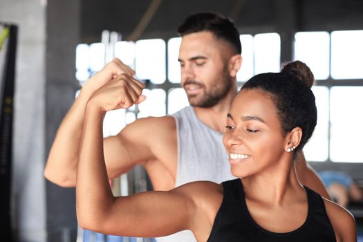 Cheerful sportive couple training together and showing biceps at the gym