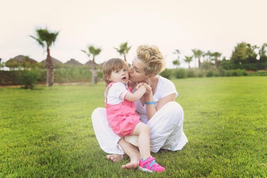 Young Mother and cute little daughter enjoying free time playing outside at backyard on the grass, happy family in nature concept